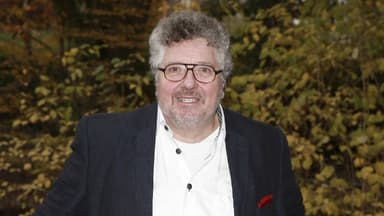 Michael Schanze im Anzug, Busch im Hintergrund