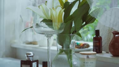 Eine Vase mit Lilien steht auf einem Brett, das über der Badewanne liegt, daneben eine Kerze und ein Parfum.