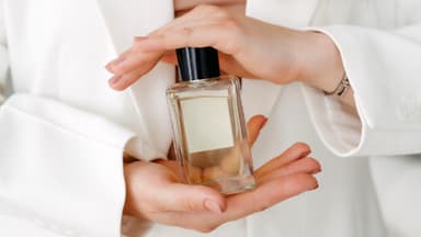 Frau hält einen Parfum-Flakon zwischen den Händen.