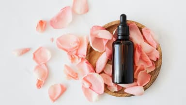 Eine Flasche mit Pipette liegt in einer Holzschale mit Rosenblättern.