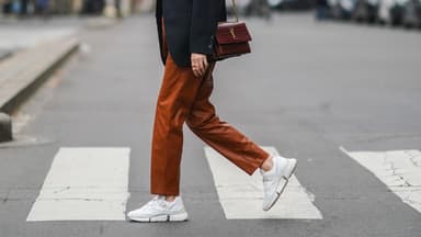 Frau mit Blazer trägt eine rötliche Hose und weiße Sneaker.