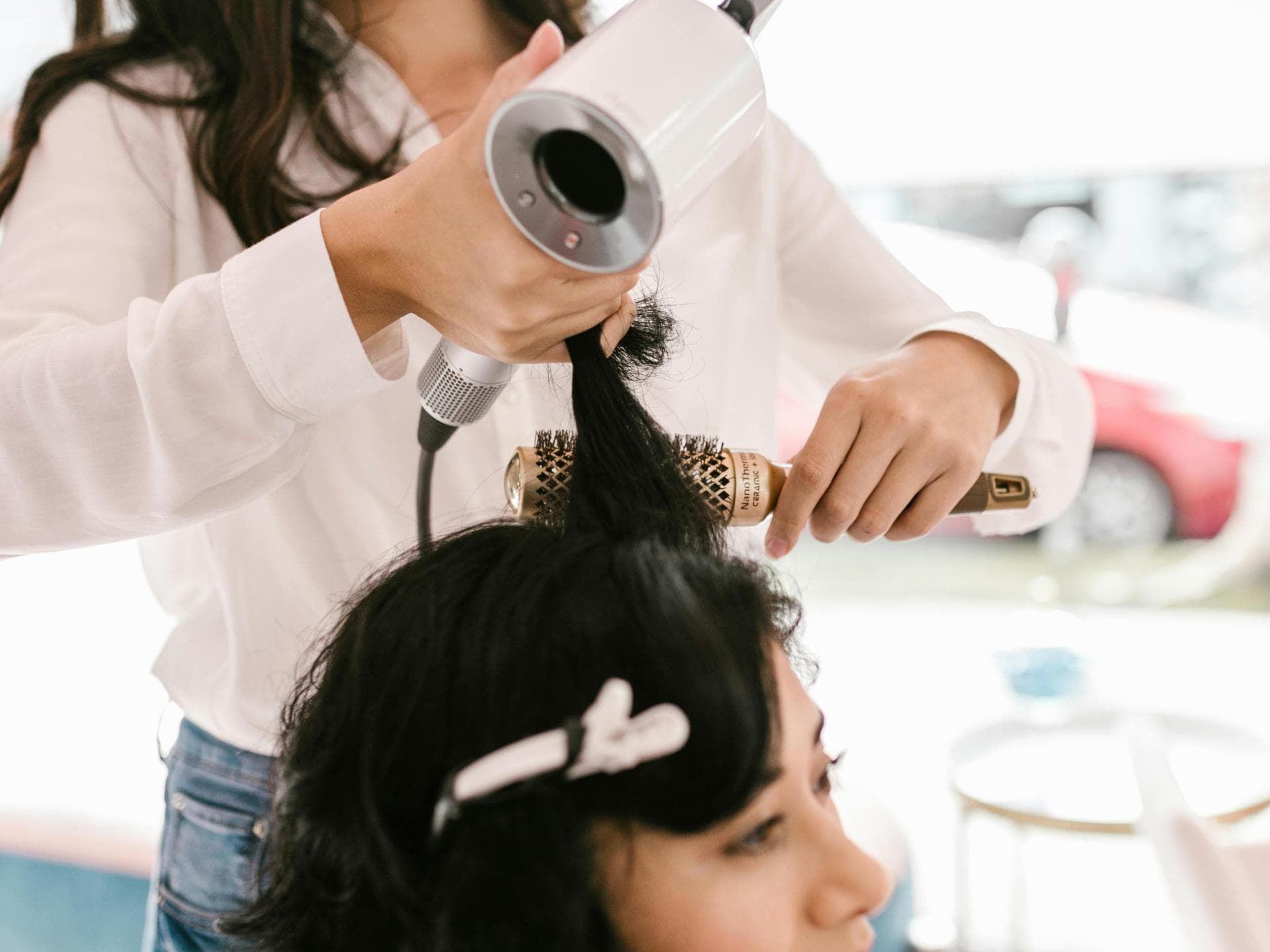 Friseurin stylt Haare der Kundin mit Föhn und Rundbürste