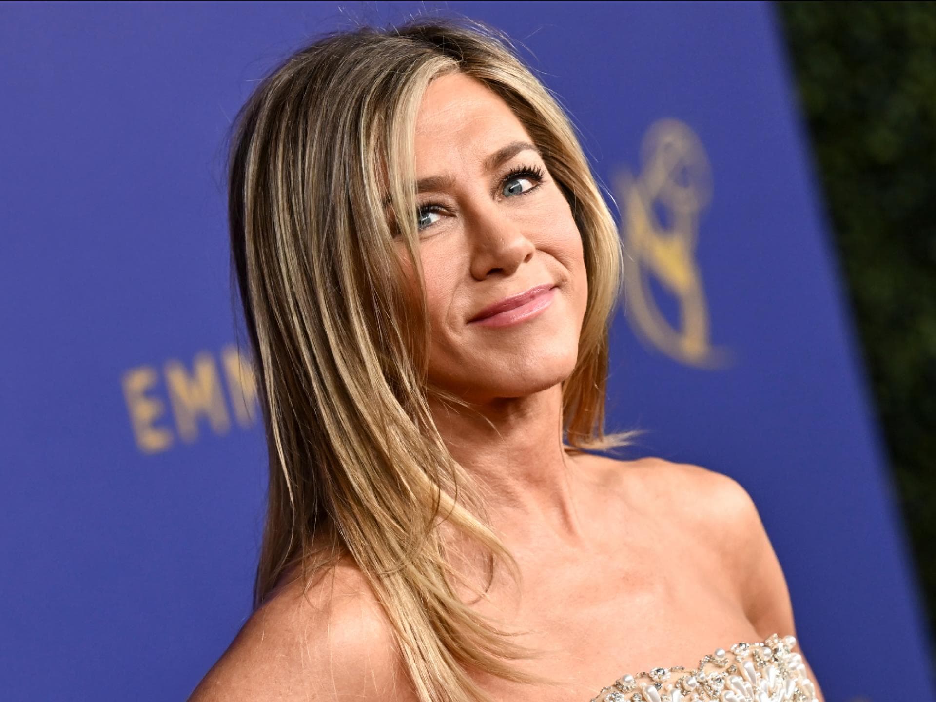 Jennifer Aniston lächelt zur Seite vor lila Wand