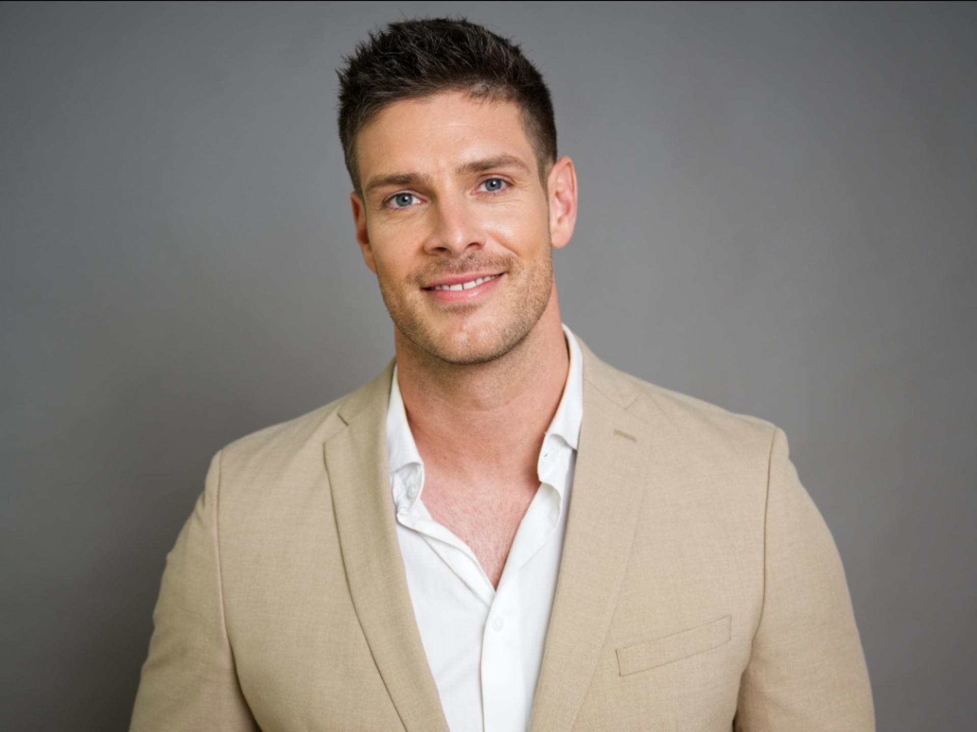 Bachelors Martin Braun im beigen Anzug vor grauer Wand