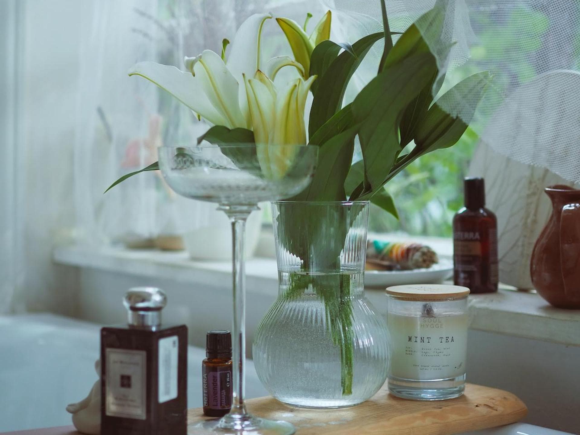Parfums mit Lilie sind jetzt wieder angesagt. Eine Vase mit Lilien steht auf einem Brett, das über der Badewanne liegt, daneben eine Kerze und ein Parfum.