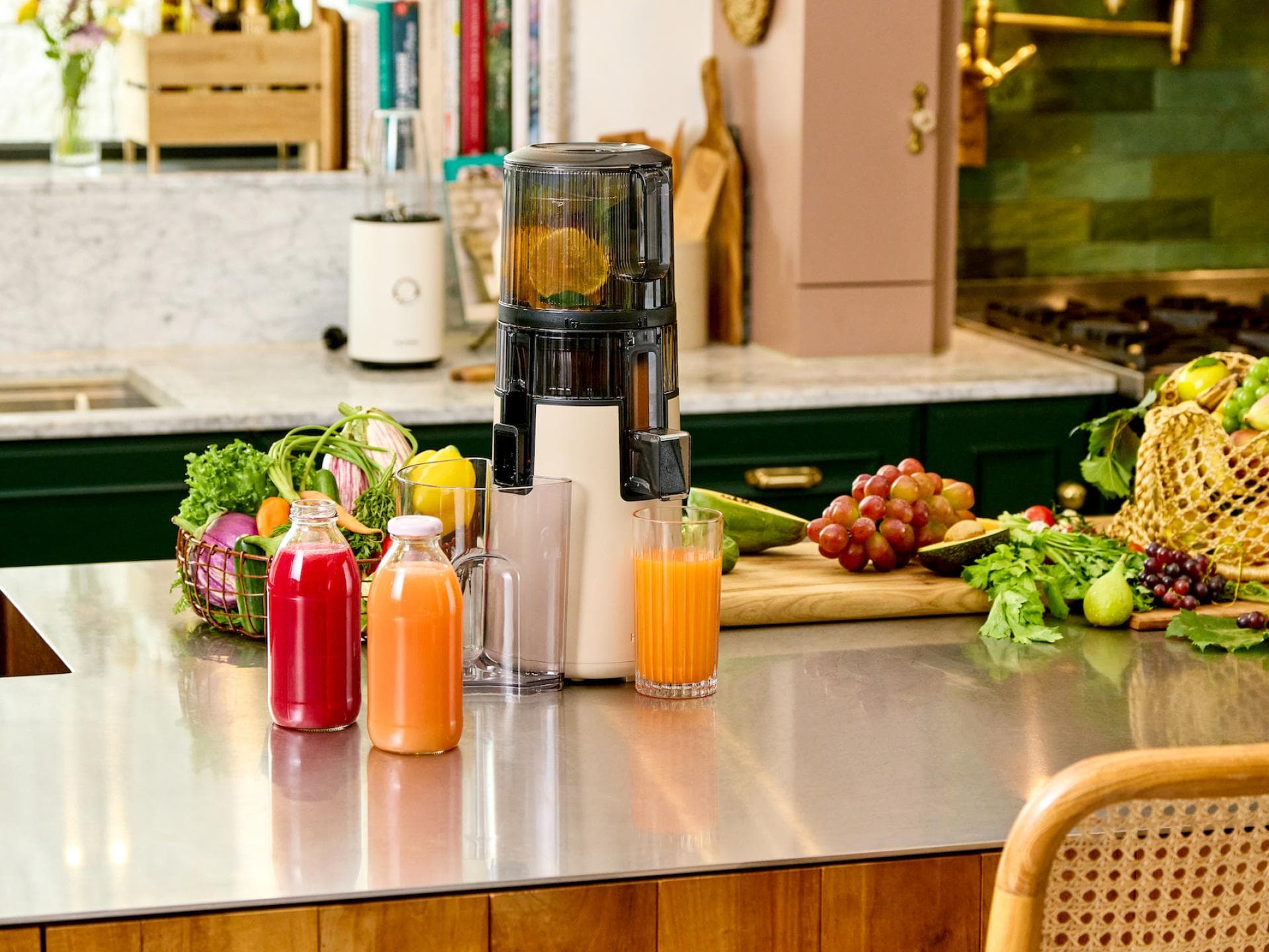 Der Slow Juicer von Hurom hilft dabei, mehr Vitamine zu sich zu nehmen. Saftpresse auf der Küchentheke, die einen frischen Saft presst. Im Hintergrund ist verschiedenes Obst.