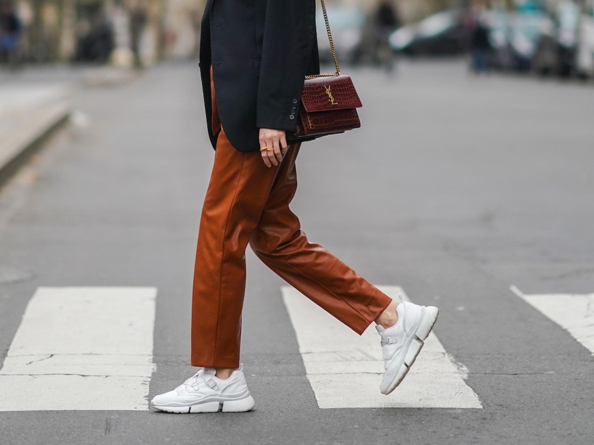 Sneaker sind bei Hallux Valgus eine gute Wahl. Frau mit Blazer trägt eine rötliche Hose und weiße Sneaker.