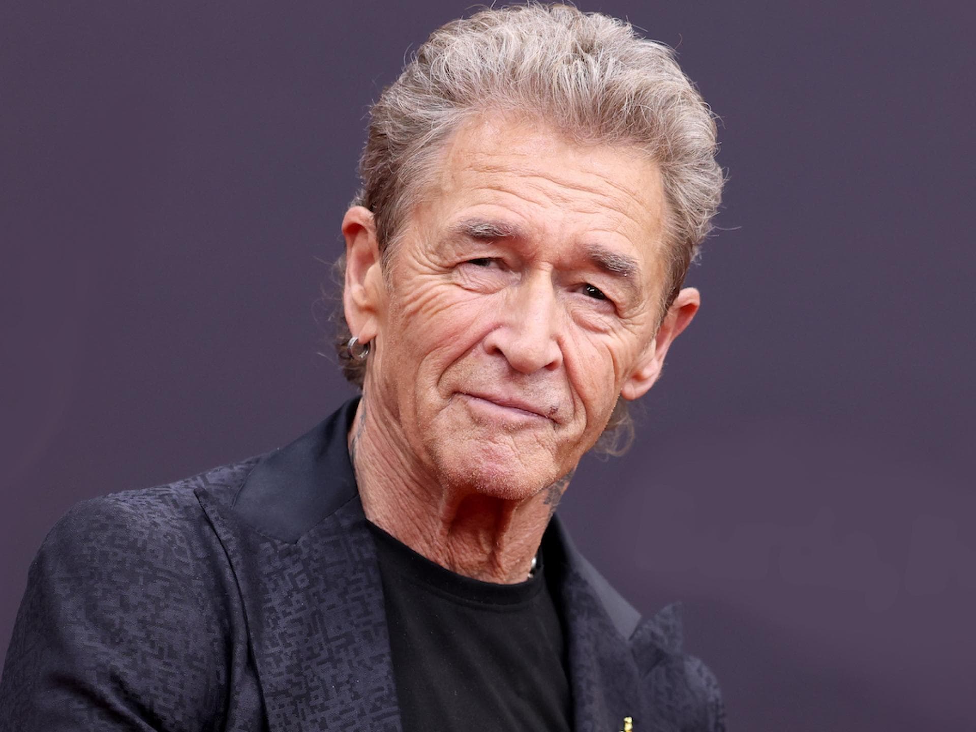 Peter Maffay guckt vor einem lila Hintergrund ernst in die Kamera
