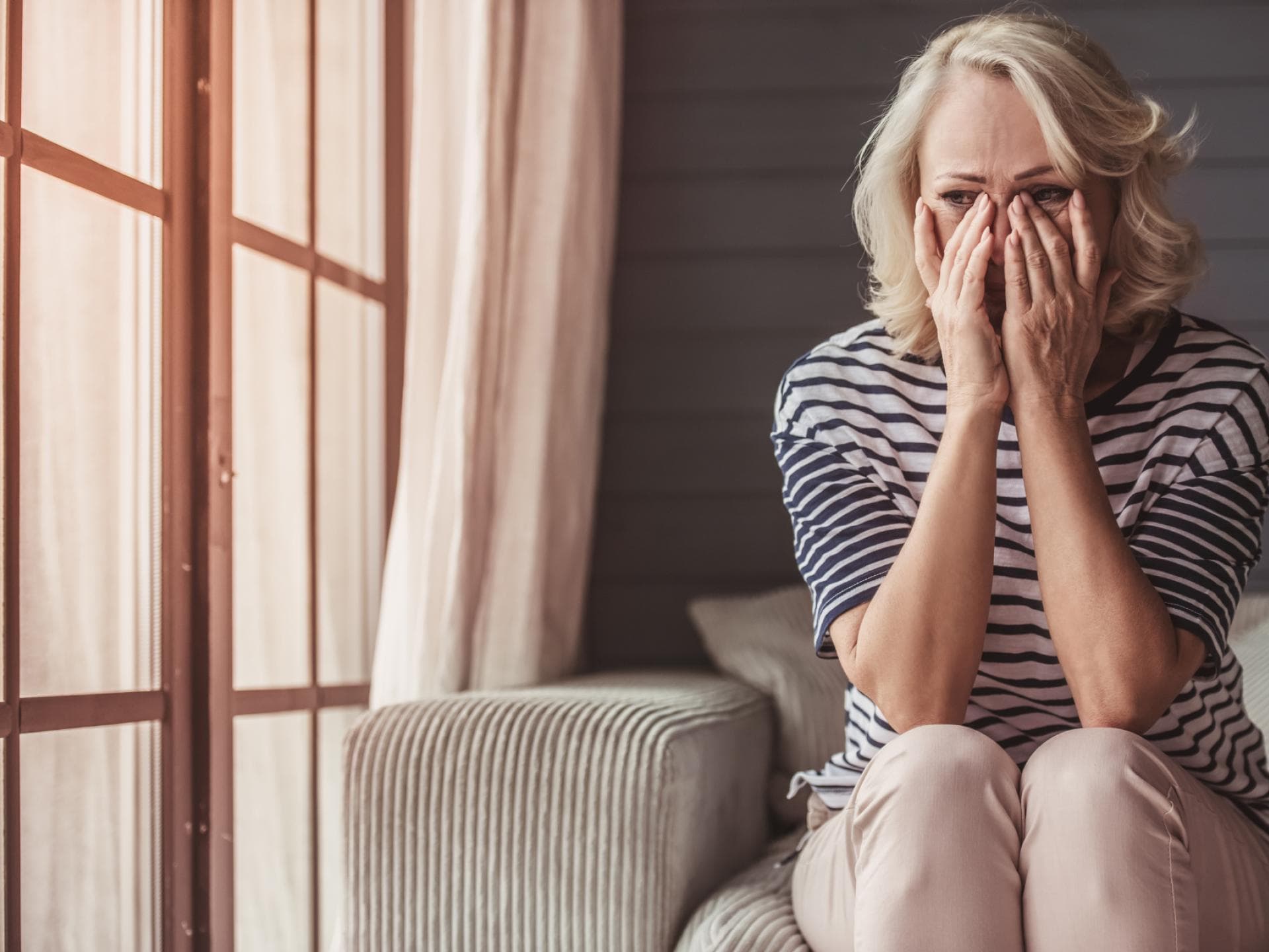Jeder Vierte in Deutschland fürchtet eine psychische Erkrankung. Frau sitzt auf dem Sofa und hält die Hände ins Gesicht.